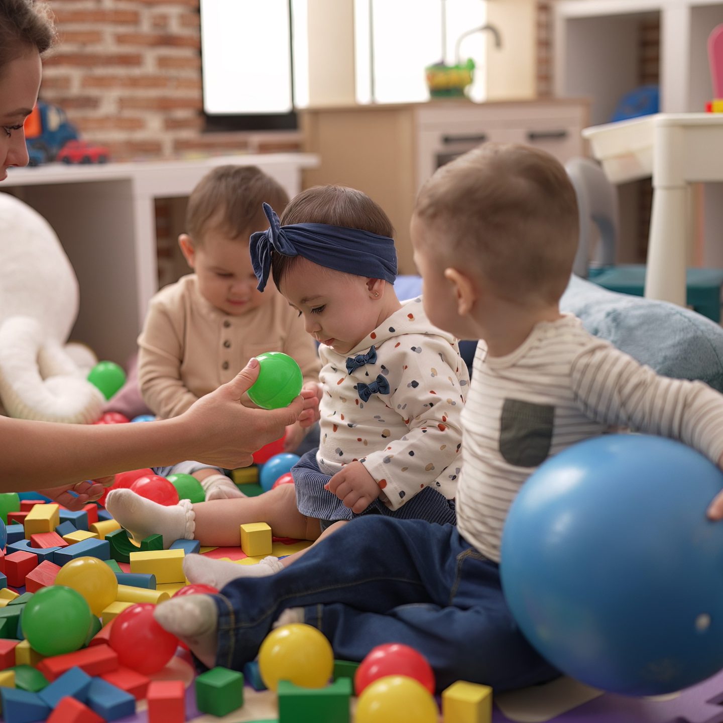Opiekunka bawi się z maluchami kolorowymi piłkami na podłodze sali