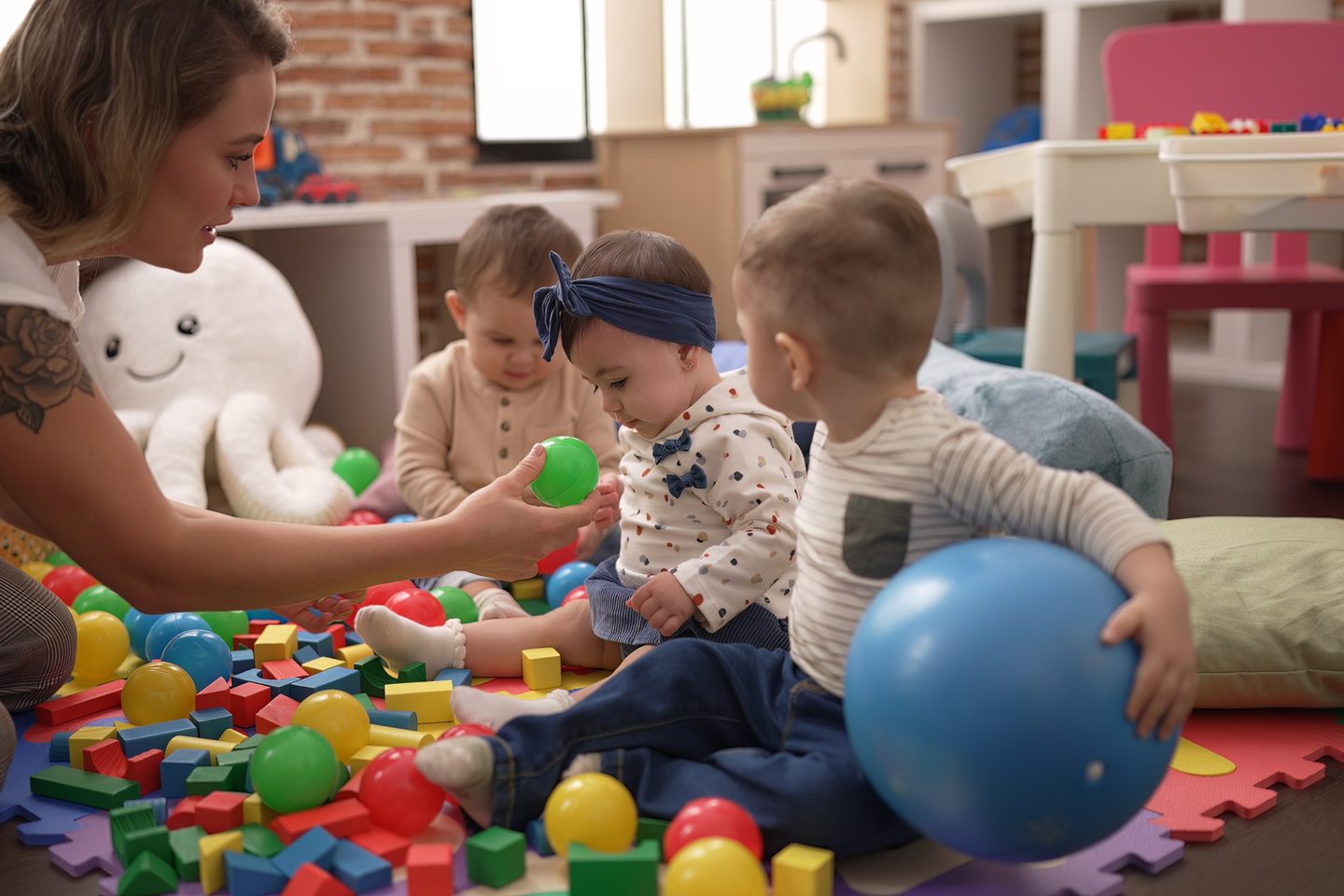 Opiekunka bawi się z maluchami kolorowymi piłkami na podłodze sali